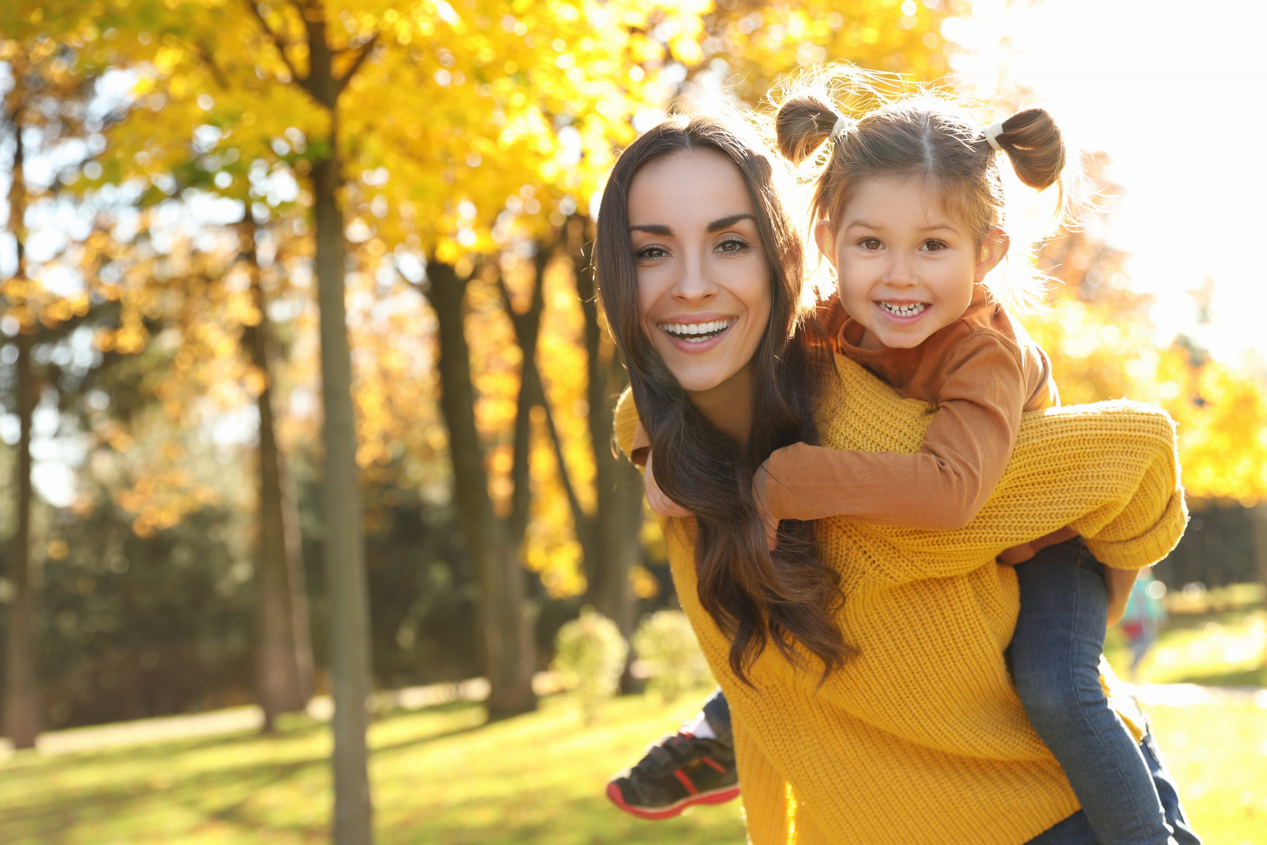 Happy woman with little daughter in sunny park. Autumn walk